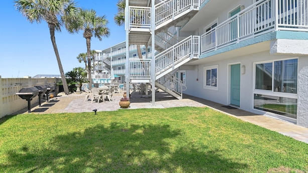 A multi-story hotel with outdoor seating, palm trees, and a clear blue sky. - Aqua Villa 302 (Fort Walton Beach)