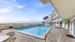 A swimming pool with lounge chairs, a table, and a building with balconies. - Aqua Villa 302 (Fort Walton Beach)