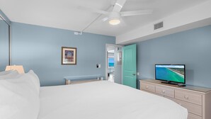 A bedroom with a bed, a television on a dresser, a ceiling fan, and a door leading to another room. - Aqua Villa 302 (Fort Walton Beach)
