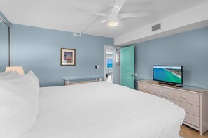 A bedroom with a bed, a television on a dresser, a ceiling fan, and a door leading to another room. - Aqua Villa 302 (Fort Walton Beach)