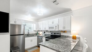 A modern kitchen with white cabinets, stainless steel appliances, and a granite countertop. - Pet-friendly Corner 1st Floor Condo in Seagrove, Steps From the Beach (Santa Rosa Beach)