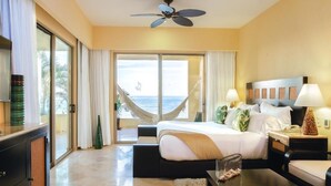 A hotel room with a bed, a desk, a chair, a nightstand, a lamp, a ceiling fan, and a view of the ocean. - Garza Blanca Resort Junior Panoramic Suite in Puerto Vallarta 1 Bedroom, 1 Bath. (Puerto Vallarta)