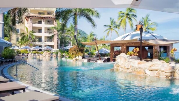 A resort pool with lounge chairs, palm trees, and a building with balconies. - Garza Blanca Resort Junior Panoramic Suite in Puerto Vallarta 1 Bedroom, 1 Bath. (Puerto Vallarta)