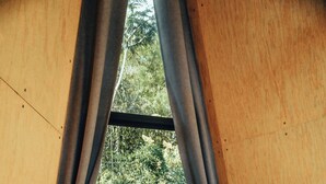 Ein Schlafzimmer mit Bett, Vorhängen, Holzboden und Blick auf Grünfläche.