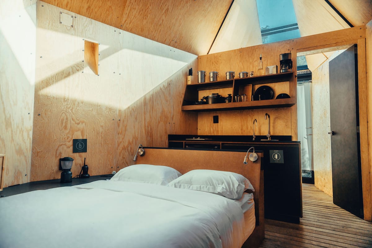 A compact, modern room with a bed, a small kitchenette, and a door leading to another space.