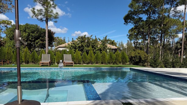 Une piscine à l’eau d’un bleu cristallin, entourée d’une pelouse bien entretenue et d’arbres.