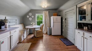 Eine kompakte Küche mit weißen Schränken, einem Kühlschrank, einem Esstisch mit Stühlen und einem Fenster mit Vorhängen.