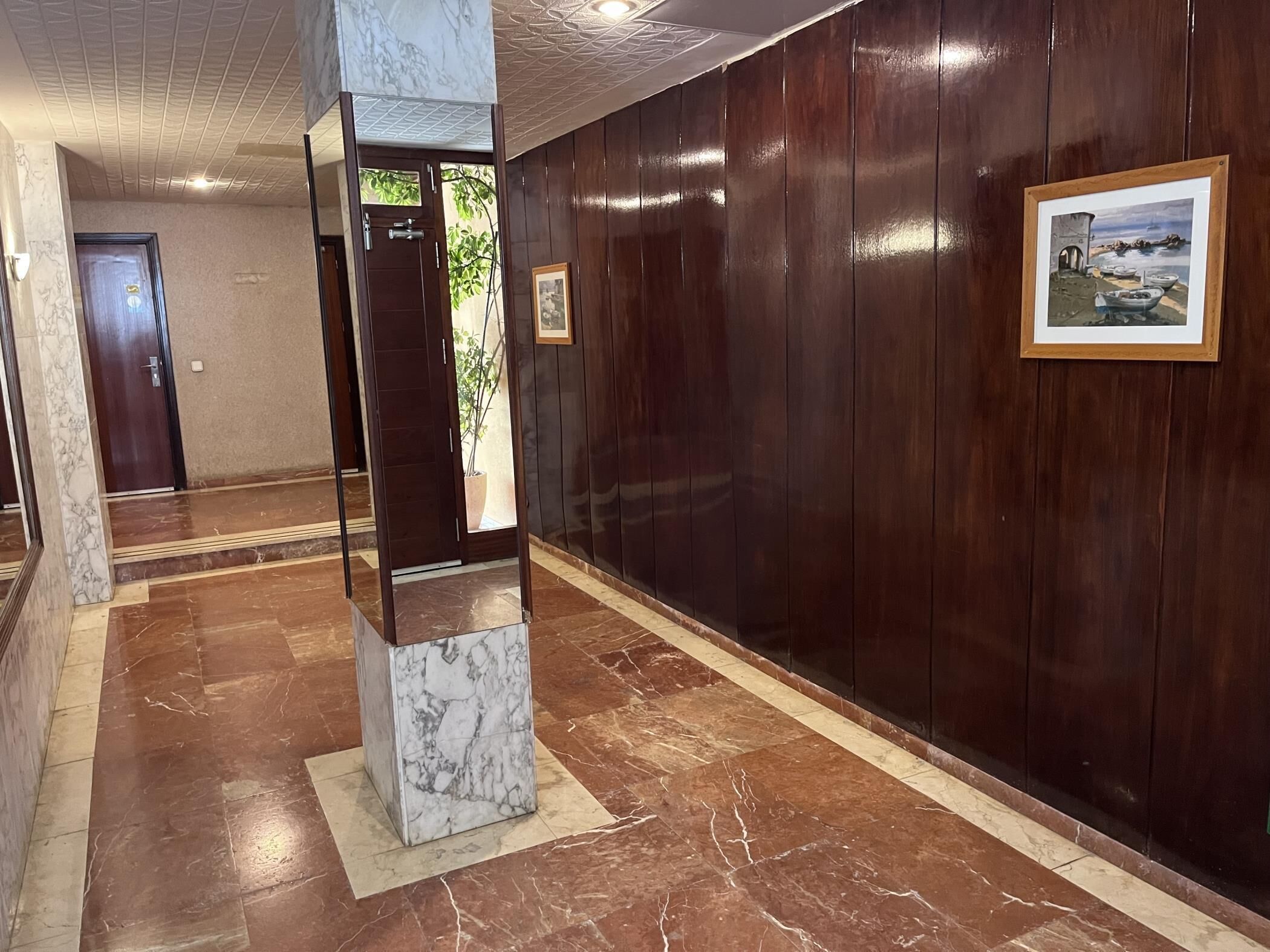 A hallway with a marble column, wooden panel walls, and a framed picture.