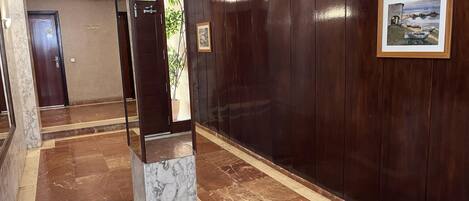 A hallway with a marble column, wooden panel walls, and a framed picture.