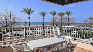 Een terras met een tafel en stoelen, een uitzicht op het strand en palmbomen.