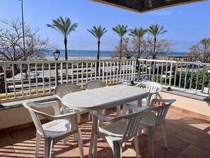 A terrace with a table and chairs, a view of the beach, and palm trees. - Beachfront apartment with spectacular sea views (Segur de Calafell)