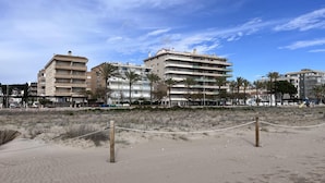 Een strand met een volleybalnet, palmbomen en meerhoogbouwwoningen op de achtergrond.