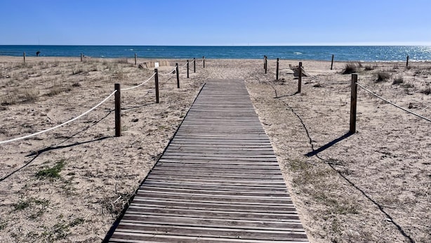Een houten looppad naar een strand, met een heldere lucht.