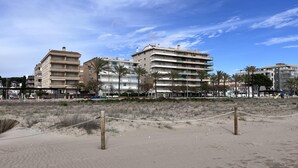 A beach with a volleyball net, palm trees, and multi-story buildings in the background. - Beachfront apartment with spectacular sea views (Segur de Calafell)