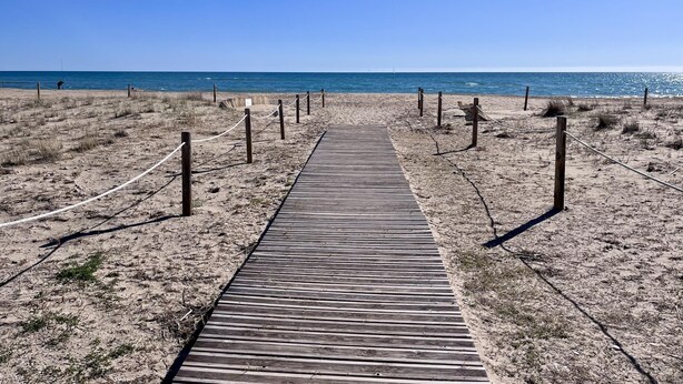A wooden boardwalk leading to a beach with a clear sky. - Beachfront apartment with spectacular sea views (Segur de Calafell)