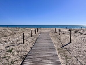 Ein hölzerner Steg führt zu einem Strand unter blauem Himmel.