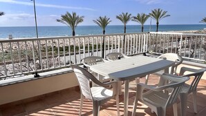 A terrace with a table and chairs, a railing, and a view of the beach and ocean. - Beachfront apartment with spectacular sea views (Segur de Calafell)
