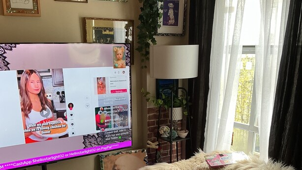 Een woonkamer met een televisie waarop een video wordt afgespeeld, een bank, een salontafel en een raam met gordijnen.
