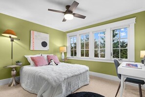 Ein Schlafzimmer mit Bett, Schreibtisch, Fenster und Deckenventilator.
