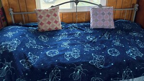 A bedroom with a bed, two patterned pillows, a window with a view of a parked car, and wooden walls.