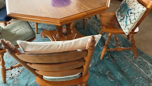 A dining table with a blue bowl, wooden chairs with cushioned seats, and a patterned rug on the floor.