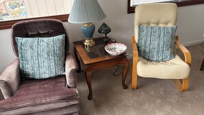 A room with two armchairs, a small table with a lamp, a decorative bowl, and a window with blinds.