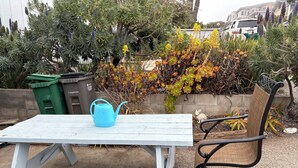 A white outdoor table with a blue watering can, a bench, and a chair.