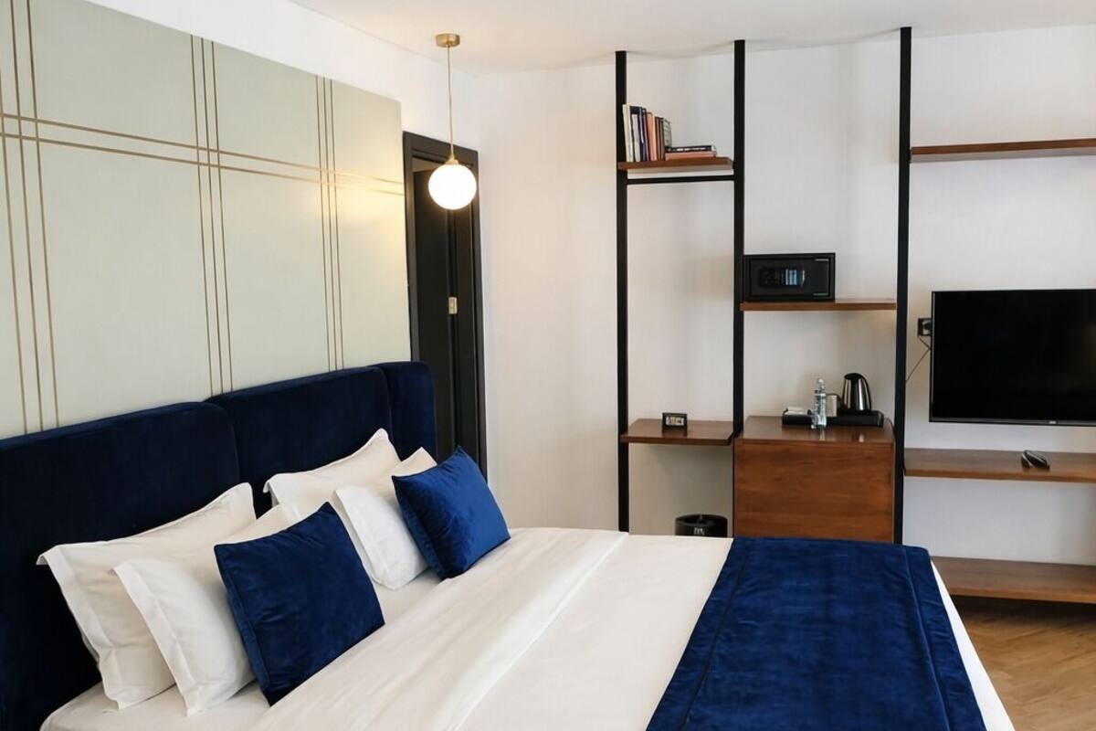 Una habitación de hotel moderna con una cama, televisión, estantería y escritorio.
