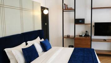 Una habitación de hotel moderna con una cama, televisión, estantería y escritorio.