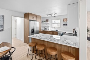 Una cocina moderna con una isla central, taburetes de bar, un refrigerador y un comedor con mesa y sillas.