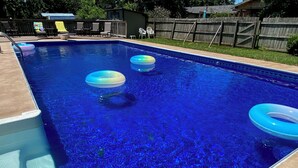 Ein rechteckiger Swimmingpool mit klarem, blauem Wasser, umgeben von einer Holzterrasse und einem eingezäunten Garten.