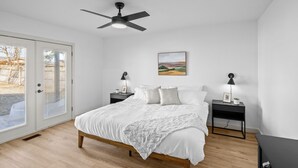 Ein Schlafzimmer mit einem Bett, zwei Nachttischen, einem Deckenventilator, einem Gemälde und einer Tür mit Blick.