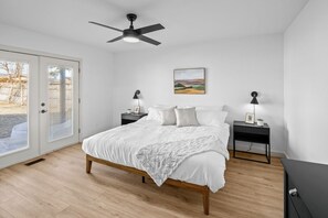 A bedroom with a bed, two bedside tables, a ceiling fan, a painting, and a door with a view. - Just Off J Street, in the heart of Bentonville (Bentonville)