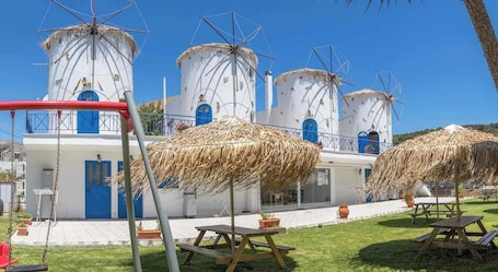 A building with white walls and blue doors, surrounded by thatched umbrellas and picnic tables.