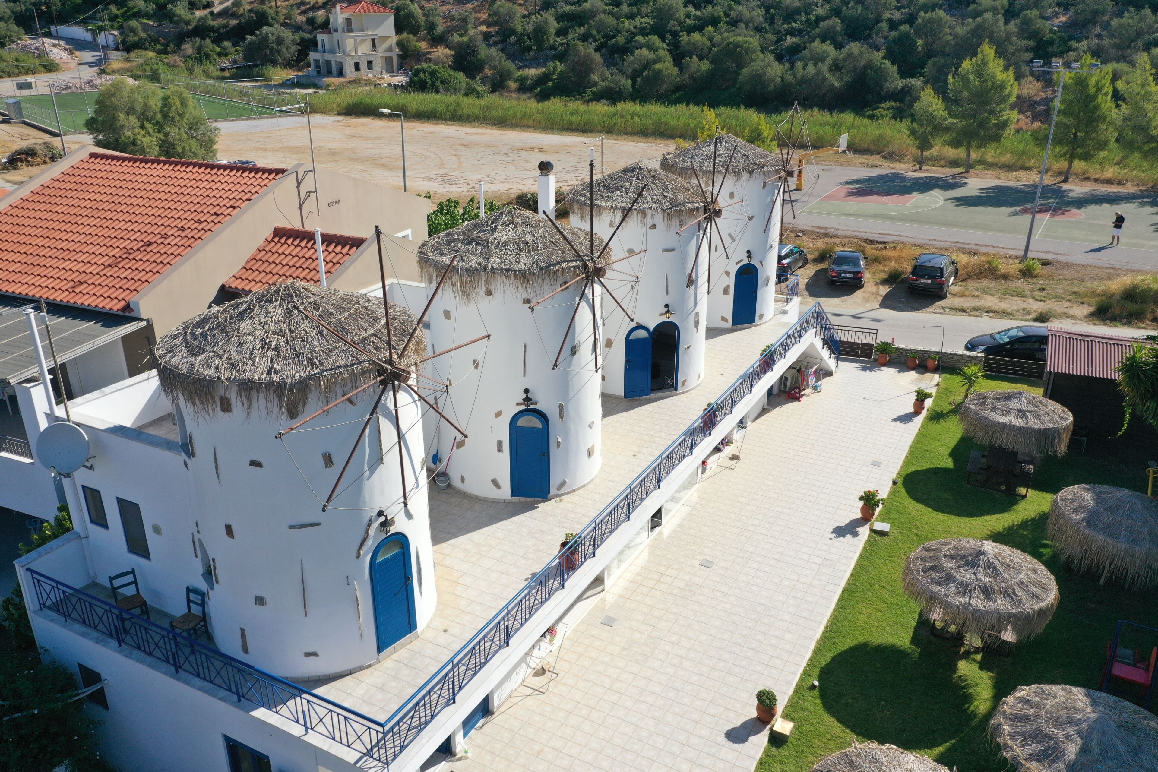 A building with cylindrical towers and blue doors, surrounded by a paved area with grass and outdoor seating.