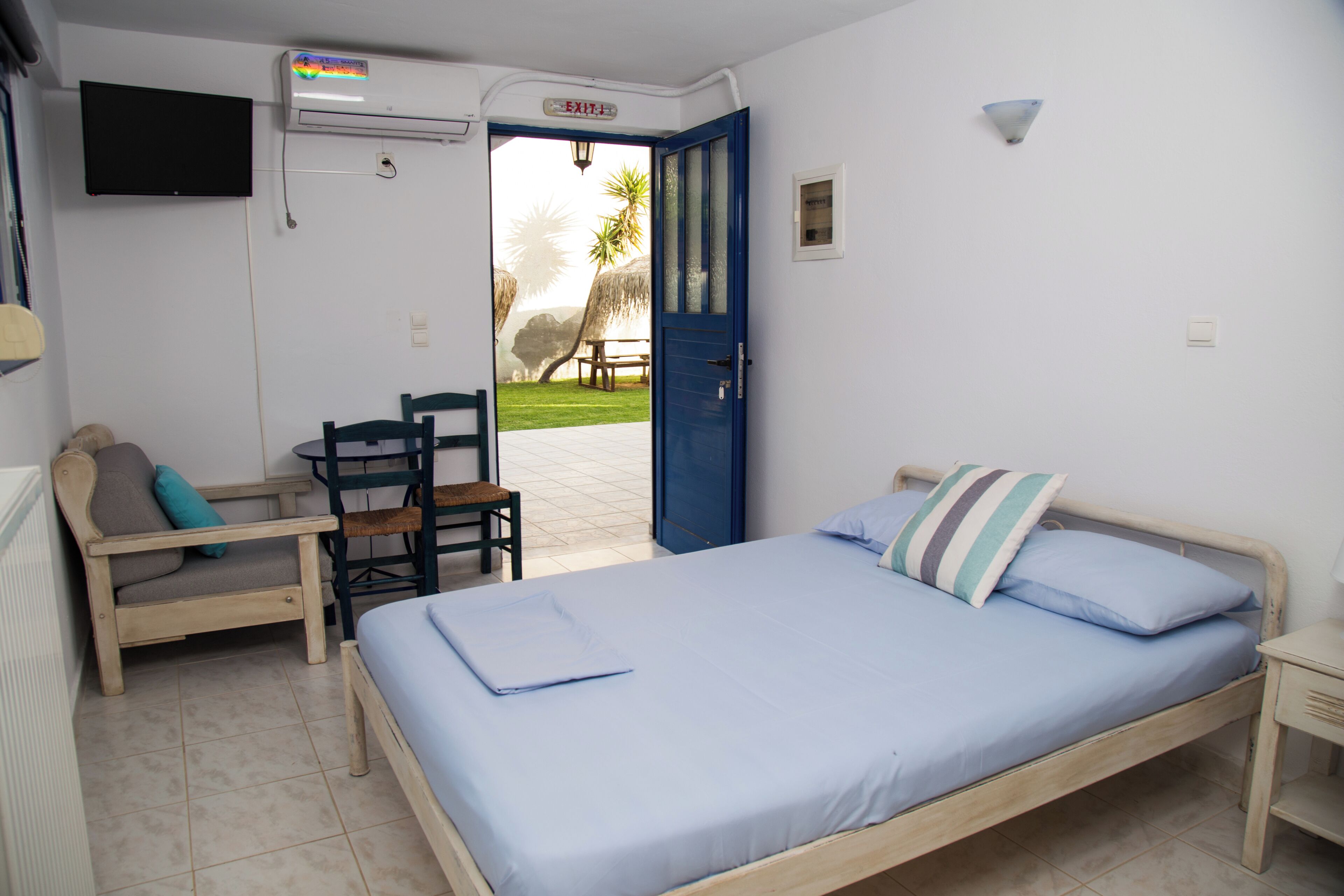 A room with a bed, a chair, a table, a TV, and an air conditioning unit.