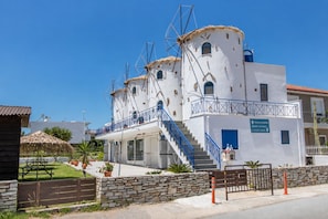 Un edificio blanco con escaleras y barandilla azul, una pequeña capilla y un letrero que indica una casa de huéspedes molino.