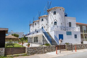 Un edificio blanco con escaleras y barandilla azul, una pequeña capilla y un letrero que indica una casa de huéspedes molino.