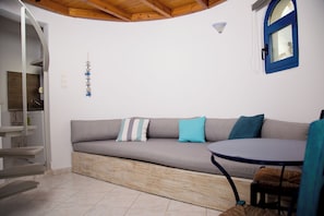 A modern interior with a grey sofa, teal cushions, a round table, and a wooden ceiling.