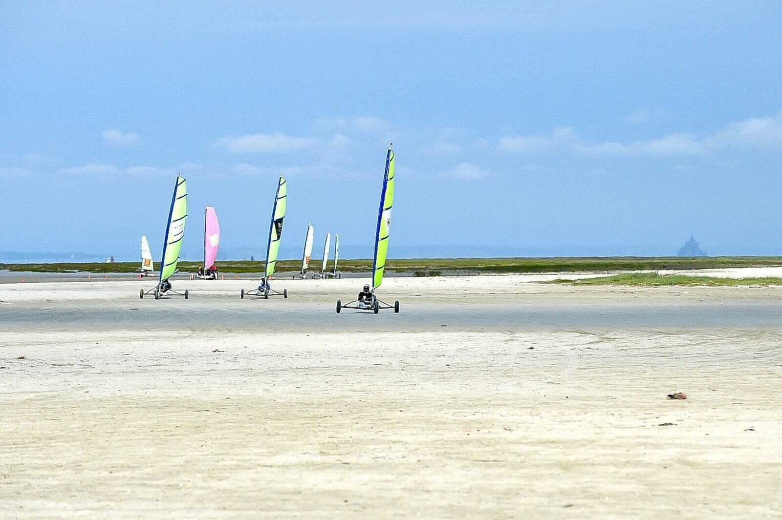 Une plage où l’on aperçoit plusieurs planches de planche à voile et, au loin, une construction.