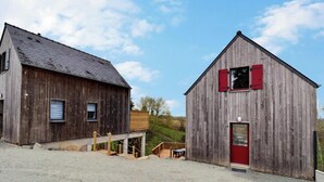 Deux bâtiments en bois, avec un sol recouvert de gravier, l’un avec une porte rouge et l’autre avec une fenêtre.