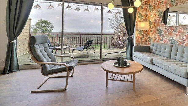Un salon comprenant un canapé, deux fauteuils, une table basse ronde et un luminaire suspendu.