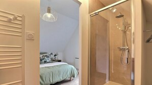 Une chambre à coucher comprenant un lit, une table de chevet, un luminaire suspendu et un espace douche doté d’une porte en verre.