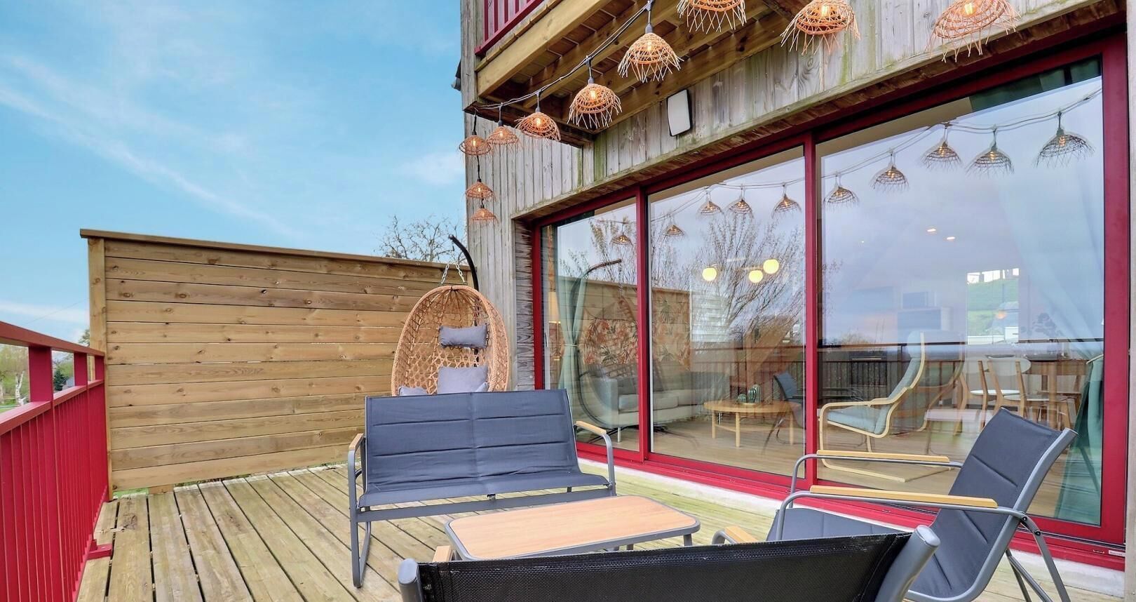 A wooden deck with outdoor seating, large windows, and hanging lights.