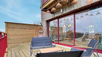 A wooden deck with outdoor seating, large windows, and hanging lights.