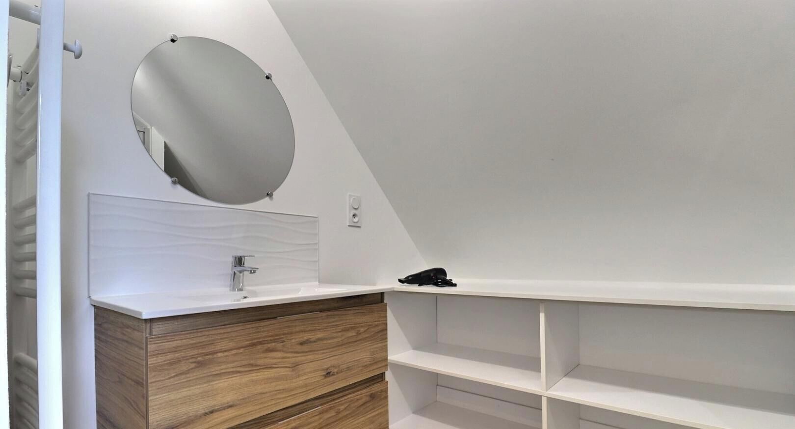 A modern bathroom with a wooden vanity, a round mirror, and a white sink.