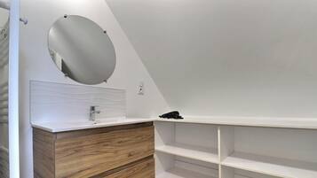 A modern bathroom with a wooden vanity, a round mirror, and a white sink.