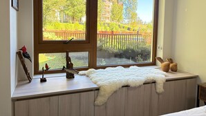 Una habitación con un ventanal grande, una alfombra blanca y mullida, un estante de madera con una escultura de pez y un cuadro enmarcado.