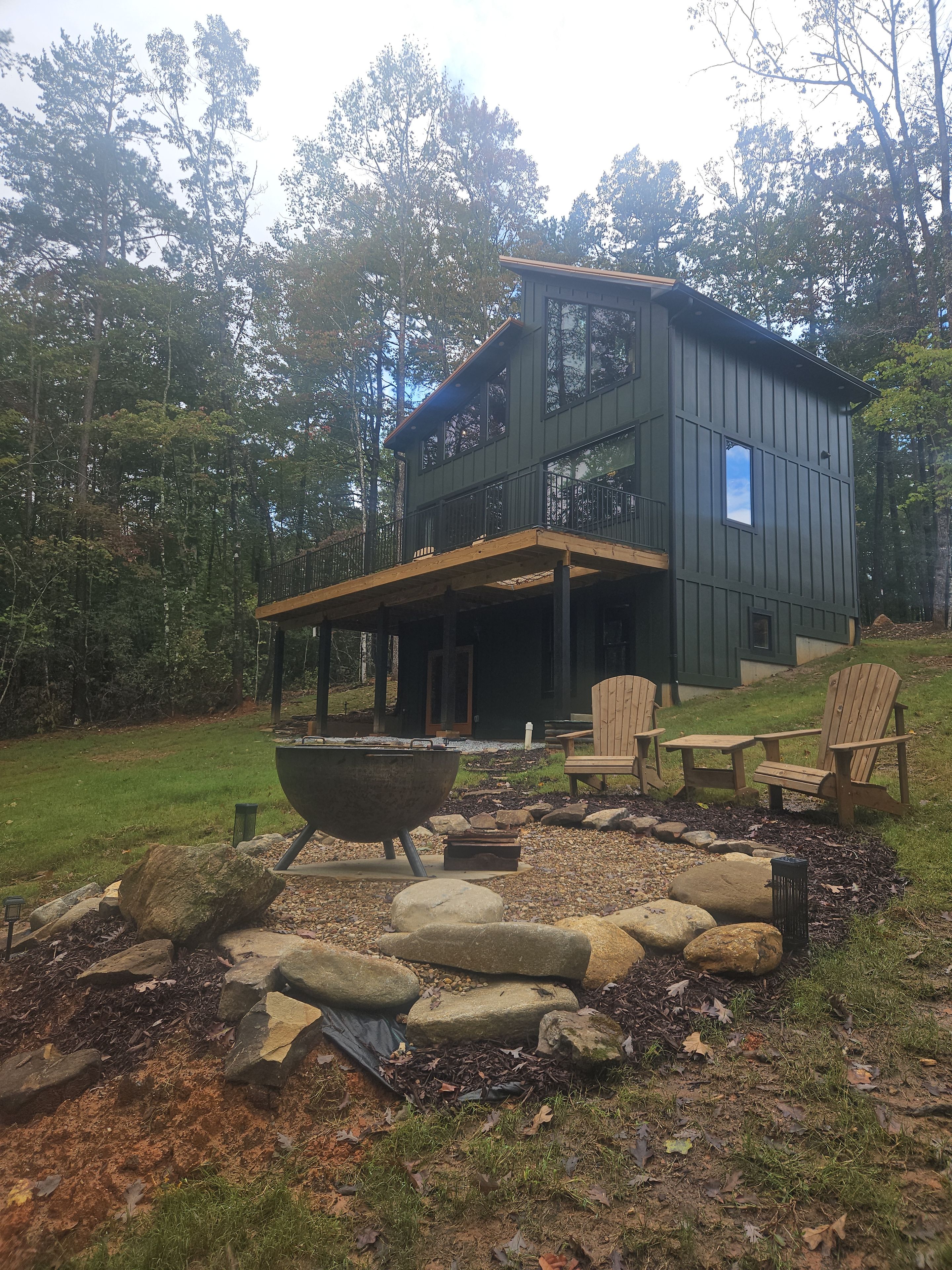 A two-story cabin with a covered patio area, outdoor seating, and a fire pit.