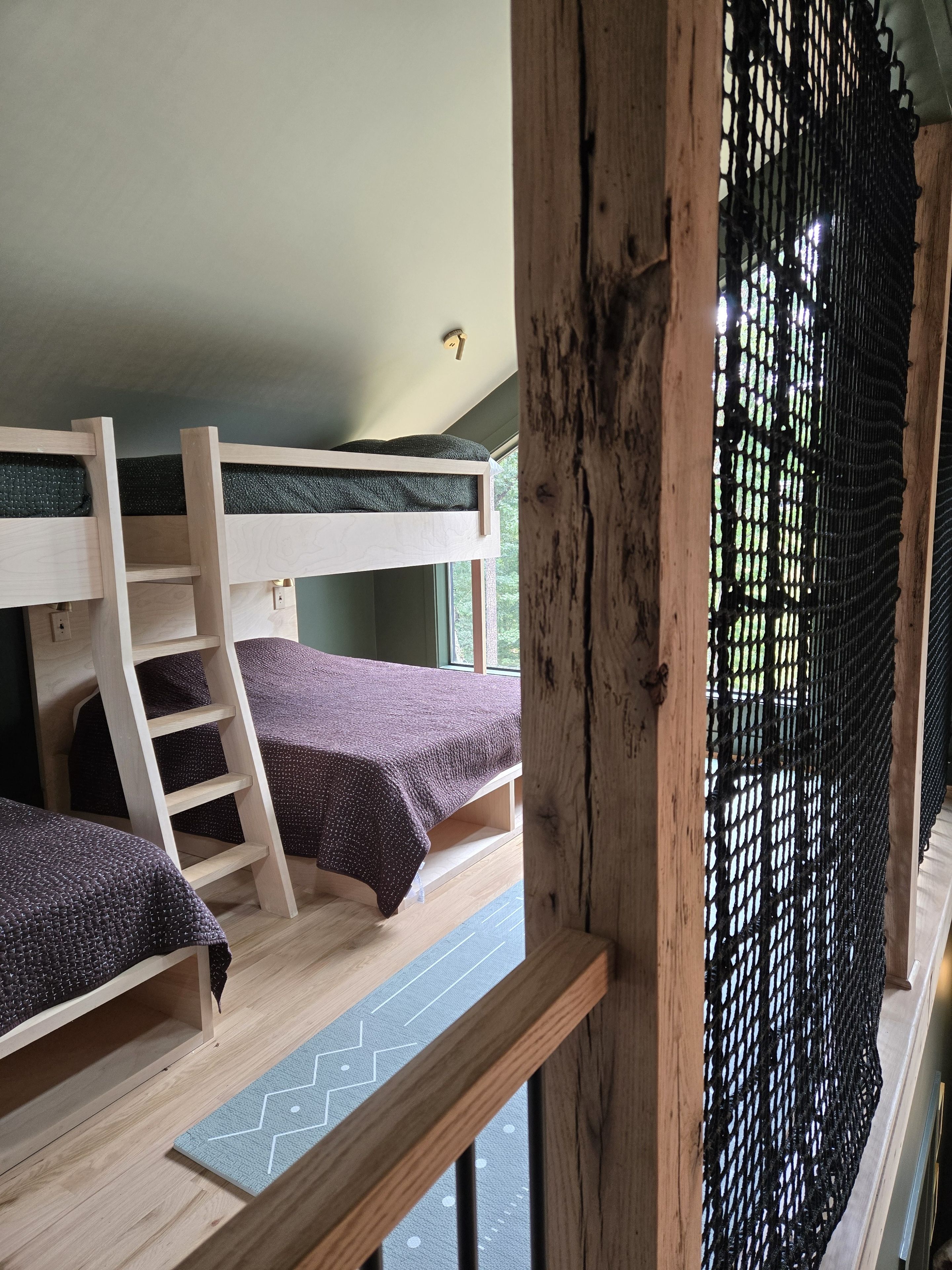 Habitación con literas, una escalera, una ventana con vistas y suelo de madera.